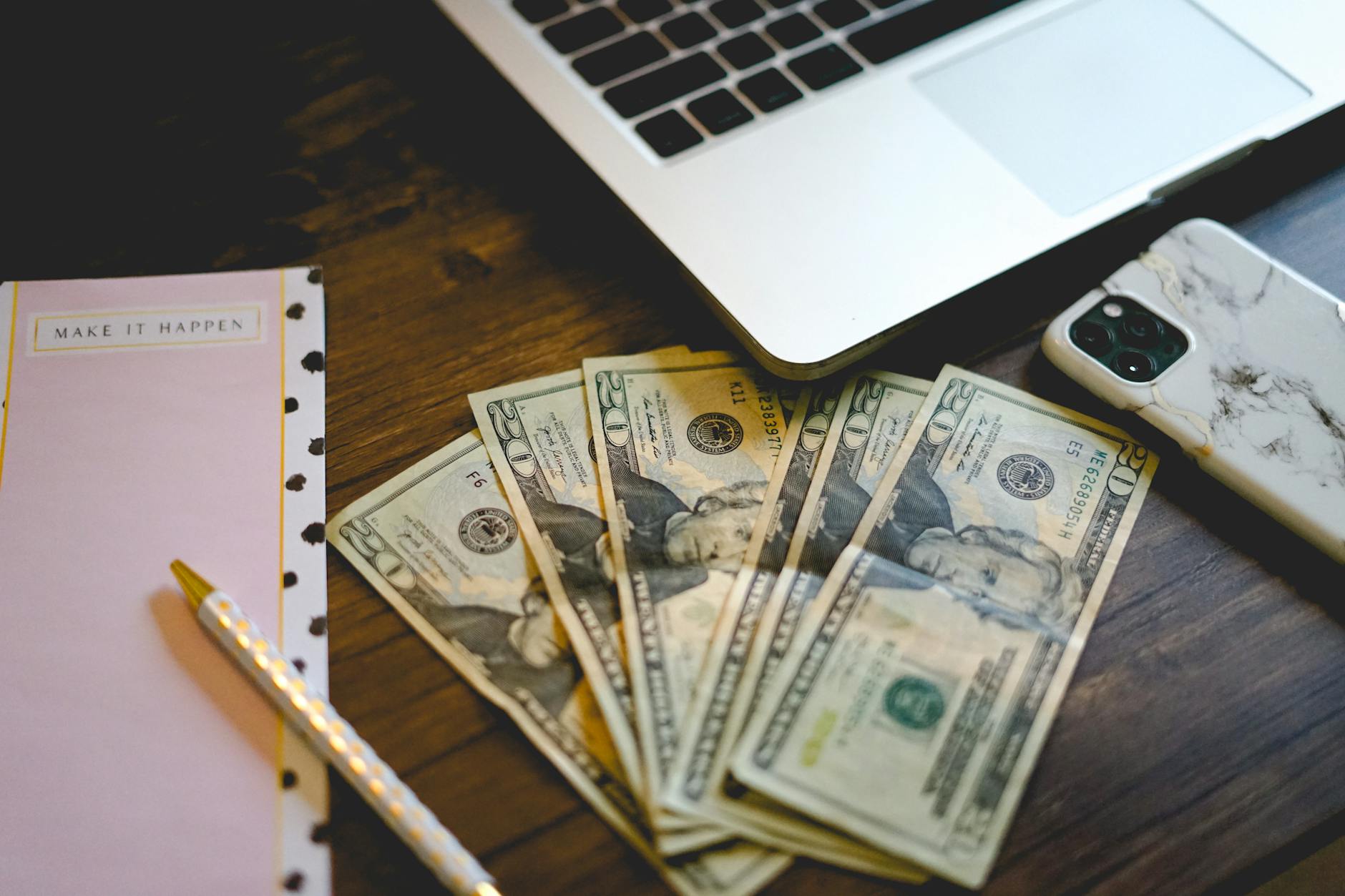 Person using laptop with cash on desk representing earning money online with free AI tools